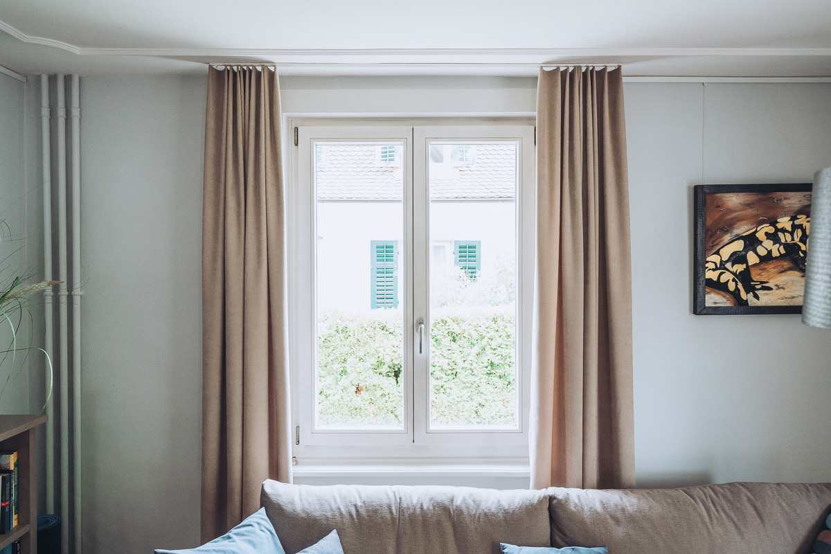 Ansicht einer Wohnungseinrichtung mit Holzm&ouml;beln, gepolstertem Sofa und Vorh&auml;ngen
